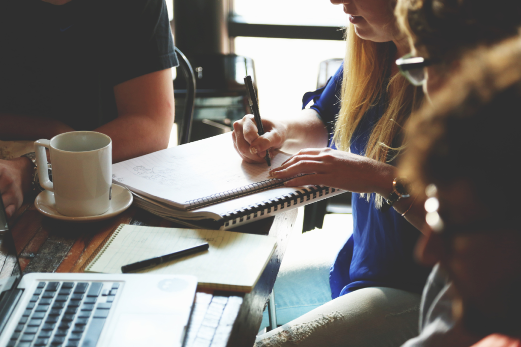 Group of people at a coffee shop with person writing on pad of paper.